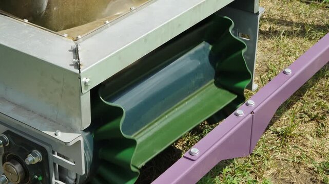 A close-up shot shows a green cleated conveyor belt with corrugated sidewalls looping around a metal roller on an industrial machine.