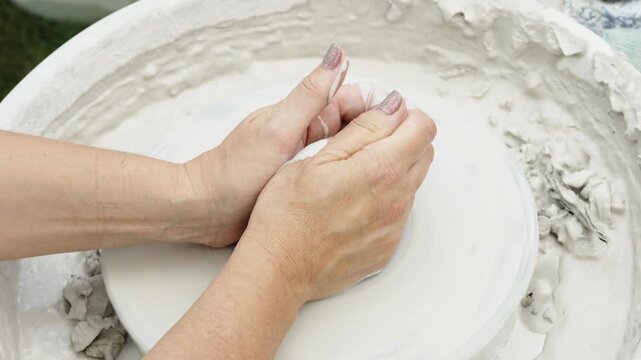 A close-up shot shows a potter's hands centering a lump of white clay on a spinning pottery wheel during a masterclass.