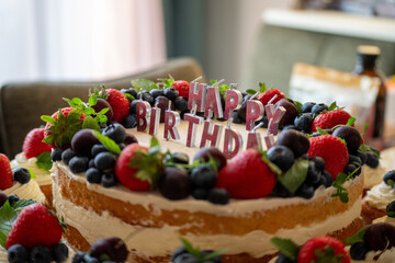 Fototapeta premium Birthday cake decorated with berries and happy birthday candles