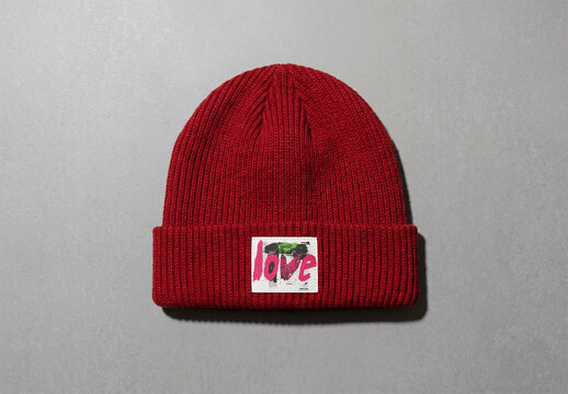 Mockup of A red beanie cap with white label sits flat on a grey surface