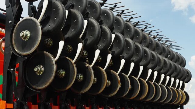 A close-up shot shows multiple rows of black double-disc coulters and press wheels on a folded modern agricultural seed drill.