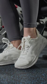 Vertical close up video of young Caucasian woman tying laces of sneakers in gym. Footage for fitness apps, sportswear commercials, and healthy lifestyle marketing campaigns