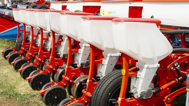 A side view shows a row of white plastic seed hoppers mounted on a modern red agricultural precision planter.