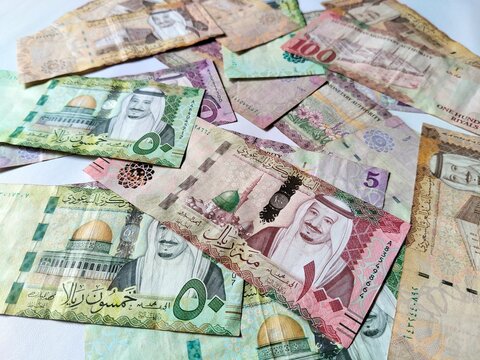 A close-up of Saudi Riyal (SAR) banknotes arranged on a white background, showing various denominations.
