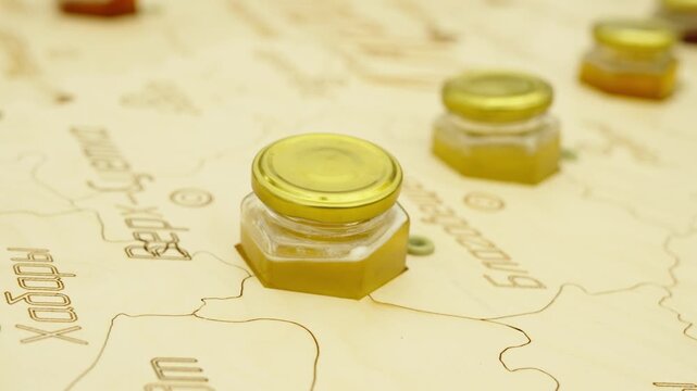 Small hexagonal honey jars are placed into a wooden map with engraved Russian district names.