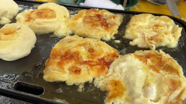 Colombian cheese arepas sizzling and melting on griddle