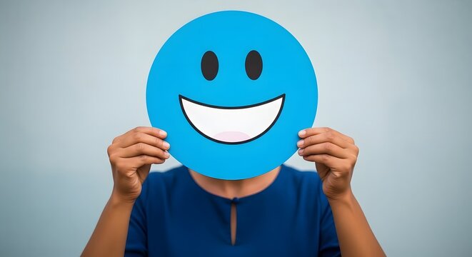 Person holding a blue smiley face sign. Happy emoji mask covering face. Positive mood concept.