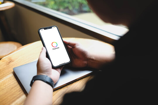 Bangkok, Thailand. July 12, 2026; A close-up view of a person holding a smartphone showing the Payoneer application logo on the screen above a closed laptop on a wooden table.
