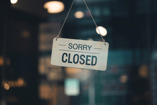 Hanging wooden sign with sorry closed text on store window at dusk.