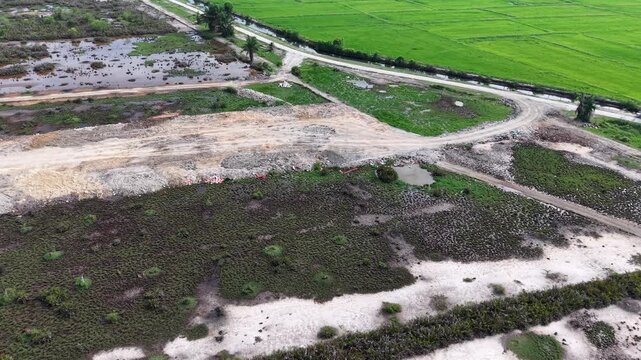 Aerial view reveals a rural landscape. Green rice fields stretch beside a winding dirt path