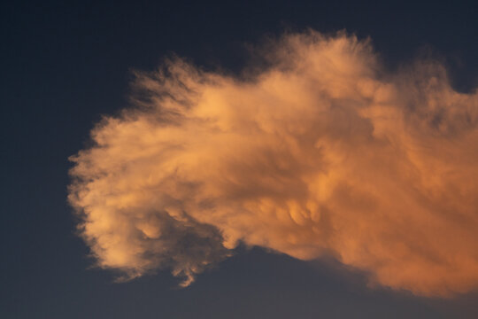 Nube de tormenta iluminada por el atardecer con tonos anaranjados sobre cielo oscuro