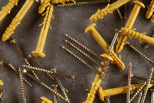 Yellow plastic dowels with metal screws on a gray background. A pile of yellow quick-installation construction dowels and metal self-tapping screws scattered on a gray textured surface. Fasteners