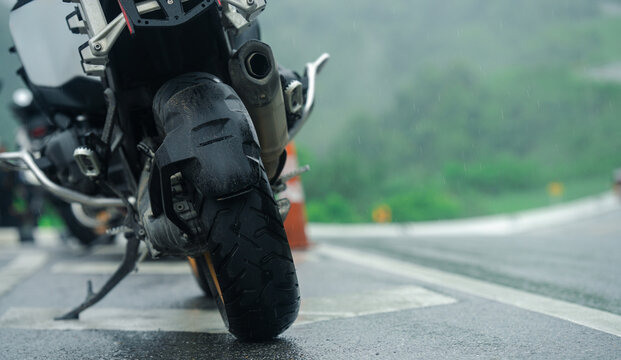 Motorcycle parked on wet road during rainy day, showcasing its rear tire and exhaust system
