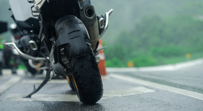 Motorcycle parked on wet road during rainy day, with focus on rear tire and blurred green landscape in background