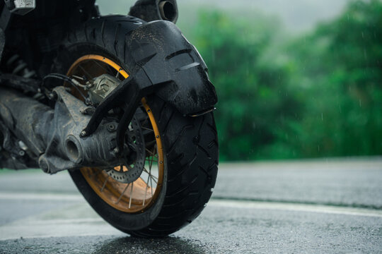 Close up of motorcycle wheel on wet road during rain, showcasing rugged tire and gold rim