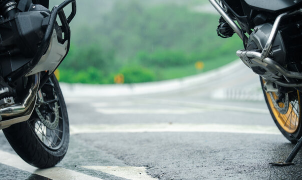Two motorcycles parked on wet road with blurred green landscape in background, evoking sense of adventure