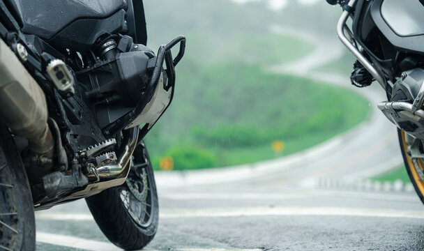 Two motorcycles parked on wet road with winding path in background, evoking sense of adventure