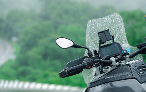 Motorcycle parked in rain with wet windshield and handlebars, surrounded by lush greenery