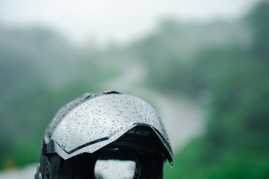 Motorcycle helmet covered in raindrops is set against blurred, rainy landscape, evoking sense of adventure and resilience