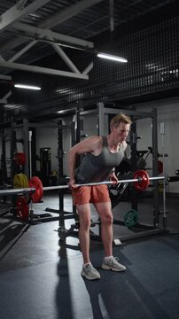 Vertical video of young Caucasian man performing barbell bent-over rows in gym. Footage for fitness center advertisements and athletic training promotions