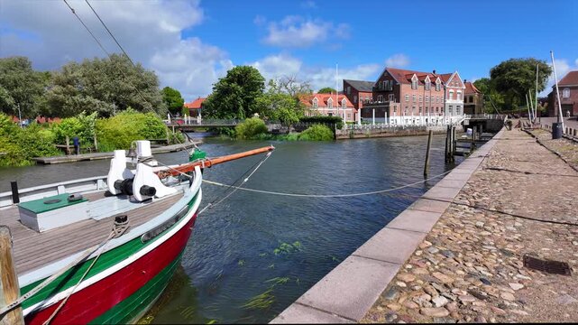 Historic harbor in Ribe with a traditional sailing ship, cobblestone promenade and historic waterfront buildings on a sunny summer day.