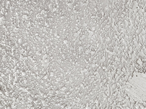 Background of uneven white acoustic wall texture with abstract grain patterns accentuates the modern industrial aesthetic. Close-up of handmade popcorn ceiling has dramatic shadows for decoration.