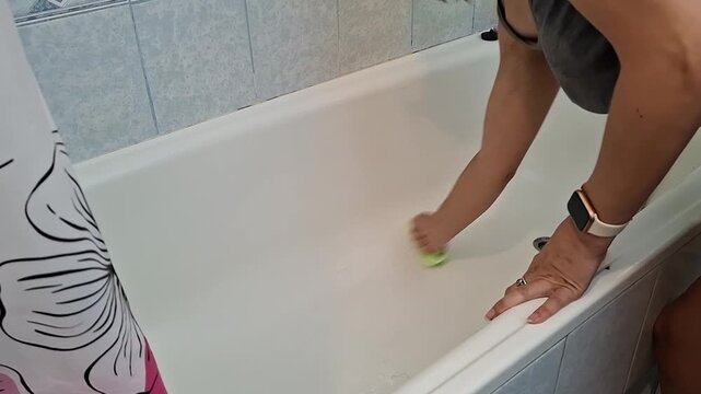 Cleaning a bathtub in a bathroom with a person scrubbing the surface in a home setting