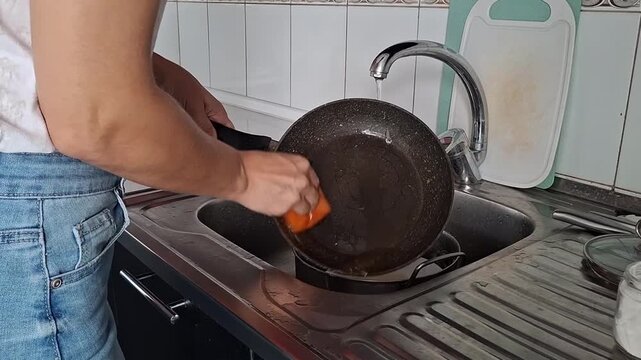 Cleaning dishes in a kitchen sink with running water in an apartment