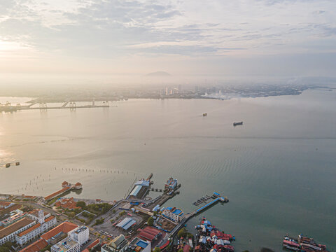 Beautiful drone landscape of George Town coastal area featuring the ferry terminal, historic clan jetties, and the misty mainland Butterworth skyline across the Penang Strait during early morning