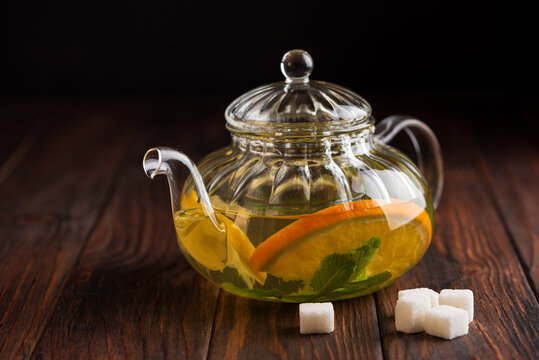 Glass teapot brewing citrus tea with orange and mint