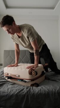 Overpacked suitcase and packing stress. Man struggling to close overloaded luggage before travel or relocation, showing common packing mistakes and authentic lifestyle, vertical