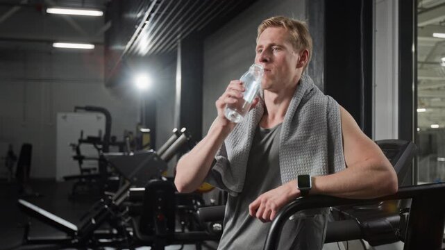 Young man drinking water and wiping sweat with towel in gym. Clip for fitness app marketing, hydration campaigns, and wellness advertisements