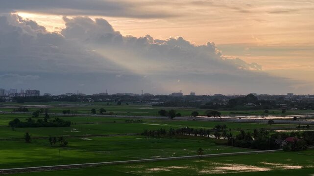 Sunbeams pierce dramatic clouds. Golden hour light softens the scene. Sunlight glint on green fields