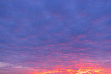 Fototapeta premium Vibrant Sunset Sky with Dramatic Purple and Orange Clouds,A breathtaking view of a dramatic sunset sky filled with textured clouds transitioning from deep purple and blue hues to glowing orange.