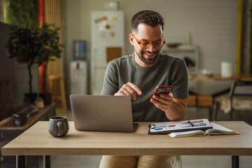 Obraz premium Smiling man using smartphone and laptop working from home