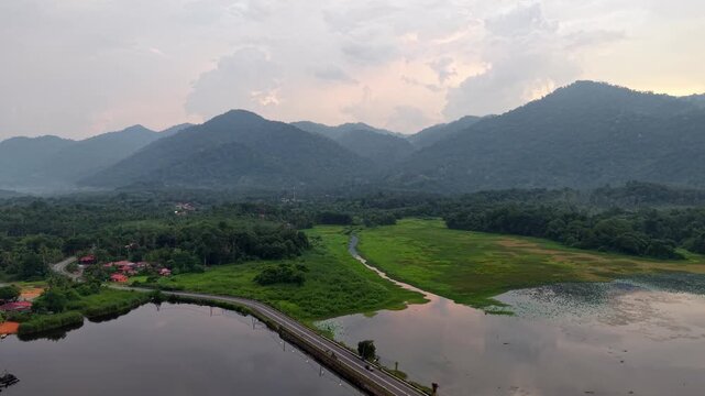 Aerial view shows mountain ranges with soft clouds. Lake and river curve through green valleys at Tasik Raban
