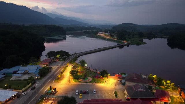 Aerial view captures a lakeside town at twilight. Mountains frame the calm lake with soft lighting at Tasik Raban