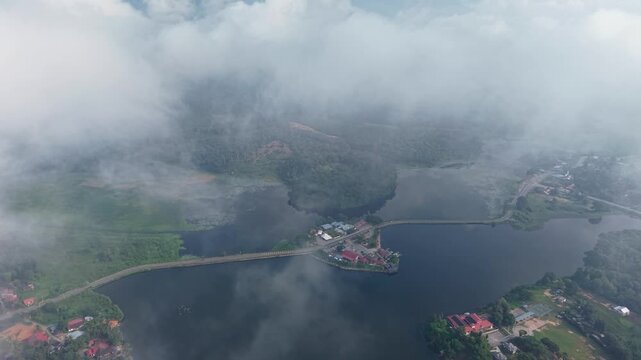Aerial view captures castle on misty lake. Thick clouds swirl around the structure and water at Tasik Raban
