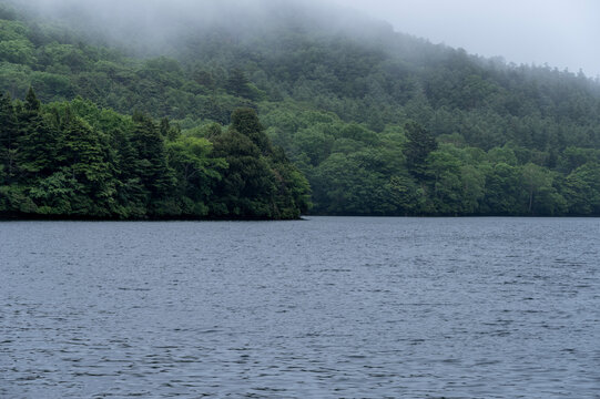 梅雨の雨が降る湯ノ湖と深緑の山々