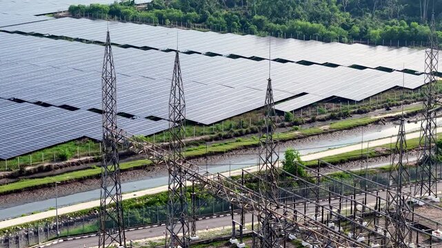 Solar panels stretch across a riverbank, rows aligned. Towering pylons stand guard