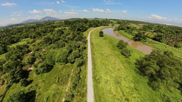 Aerial fisheye view shows a straight road through lush green fields. River flows parallel to the path
