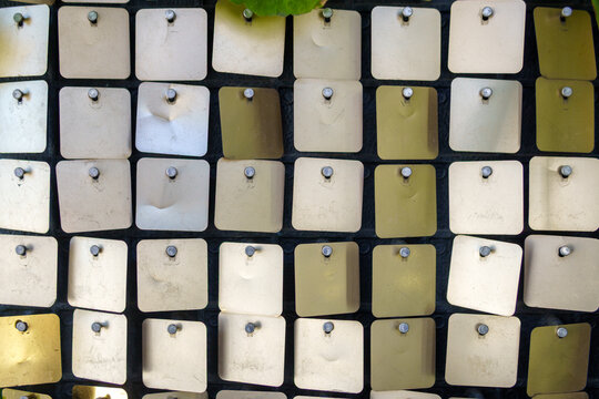 Small square metal sequins fixed with pins on a dark background. Shimmering matrix wall panel texture with silver and gold metallic pieces.