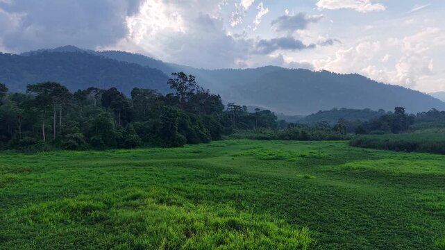 Green fields stretch toward distant mountains. Water reflects clouds and sky at Tasik Raban