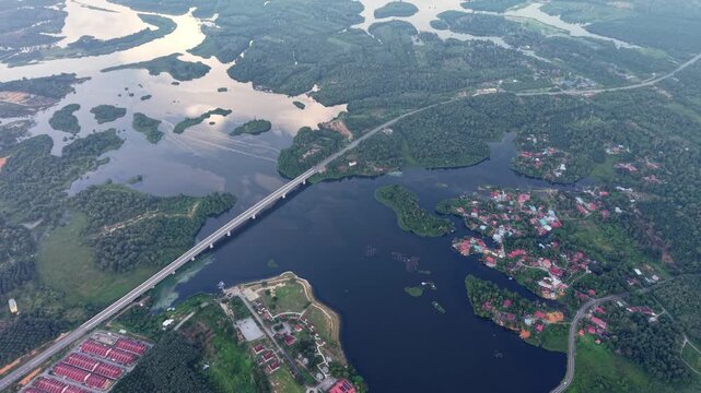 Aerial river with a bridge, surrounded by green forest, rural houses, and roads at Tasik Raban