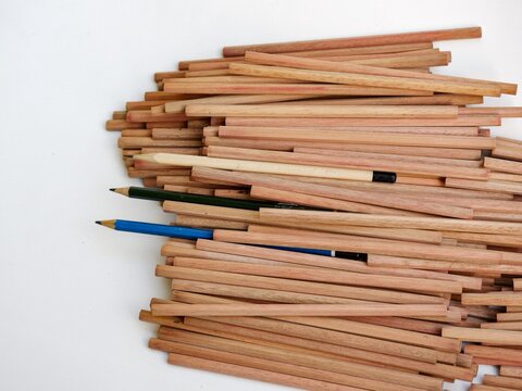 Vibrant pops of blue and green break the monochromatic texture of a clean, structured pile of raw organic wooden sticks on a white backdrop.