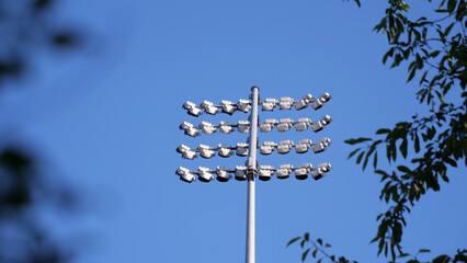 Stadium floodlights, arena lighting tower, stadium light pole against blue sky background, professional sports illumination infrastructure, soccer field lights © Adrenaloby