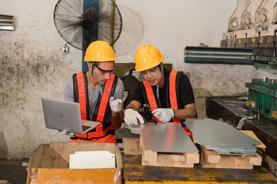 Machine operator measuring sheet metal part with caliper beside factory floor fan