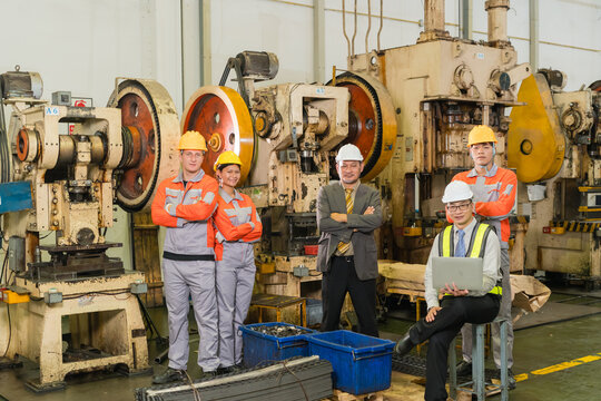 Press operators and plant manager pose near parts bins beside heavy stamping machinery