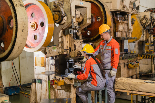 Male supervisor guiding female operator using automatic power press in metal stamping row