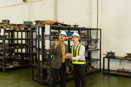Senior Manager And Engineer Reviewing Overhead Equipment Near Metal Die Storage Racks